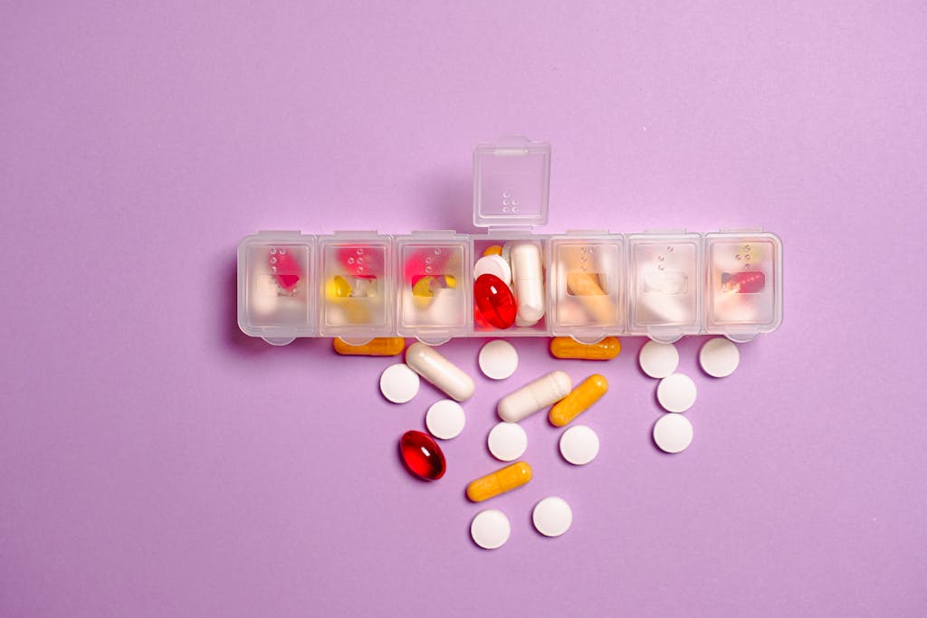 Variety of pills and capsules spilling from a clear weekly pill organizer on a purple surface.